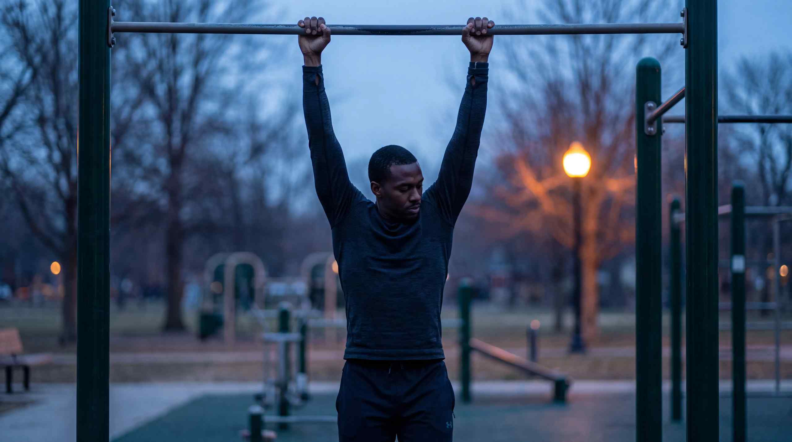 A man hangs on a bar in a park.